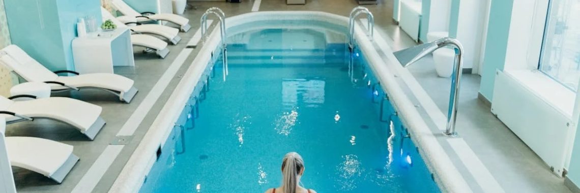 A woman in a red swimsuit prepares to enter an elegant indoor pool at a luxurious spa.
